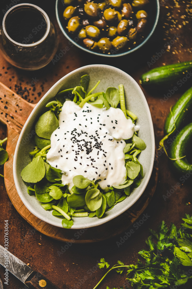 Turkish starter, meze dish. Bowl of fresh green purslane salad with yogurt, black sesame over rusty 