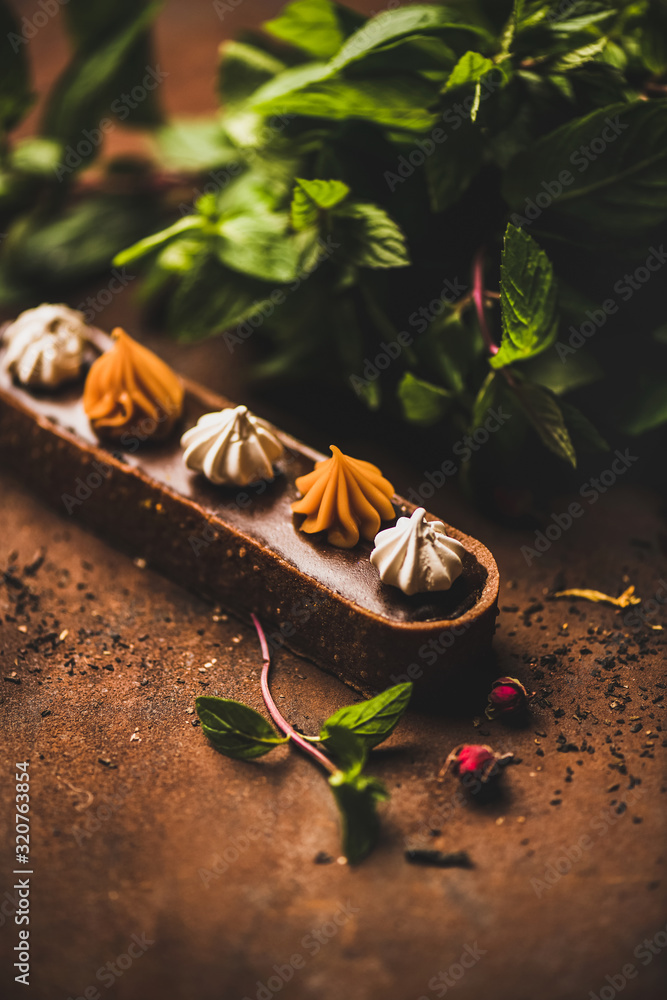 Contemporary dessert. Belgian chocolate, Swiss merenge and caramel tart with fresh mint leaves over 