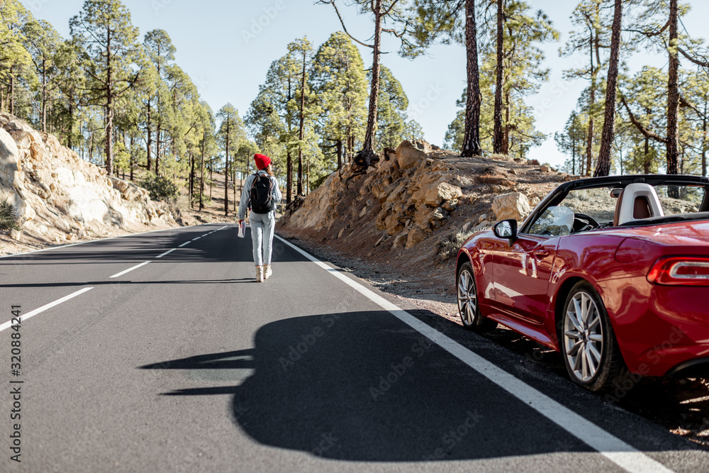 Carefree woman walking on the mountain road, traveling on a beautiful sports car