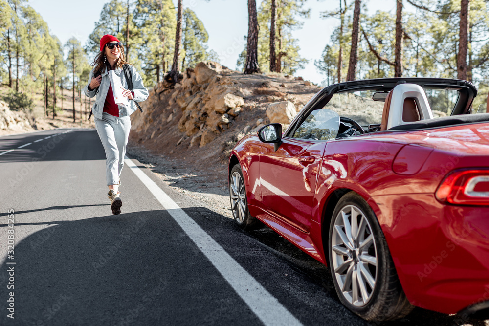 Carefree woman walking on the mountain road, traveling on a beautiful sports car