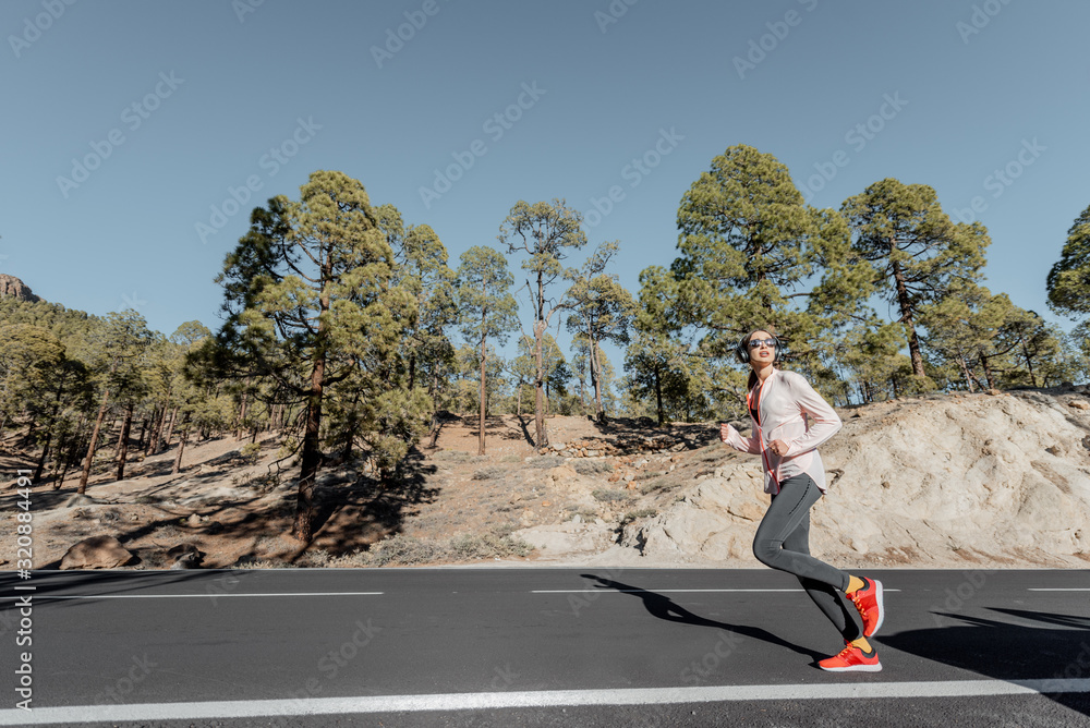 Young woman in sportswear jogging on the beautiful mountain road in the forest, wide view from the s