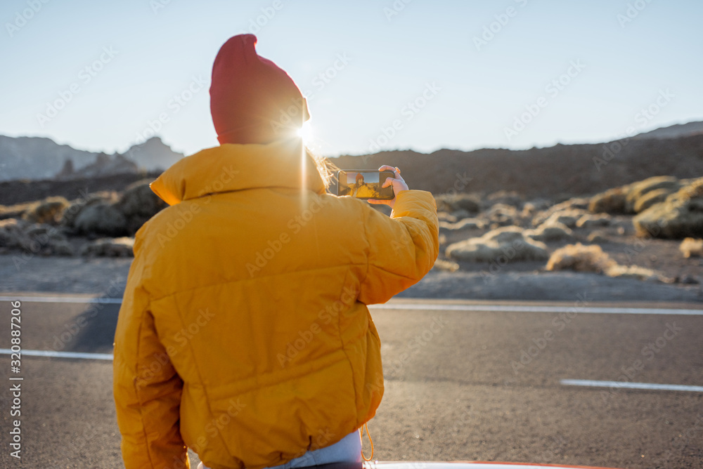 Woman enjoying beautiful volcanic landscapes, photographing on phone on the roadside during a sunset