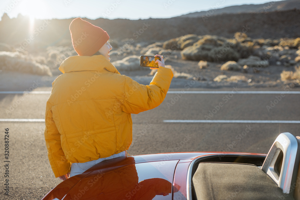 Woman enjoying beautiful volcanic landscapes, photographing on phone on the roadside during a sunset