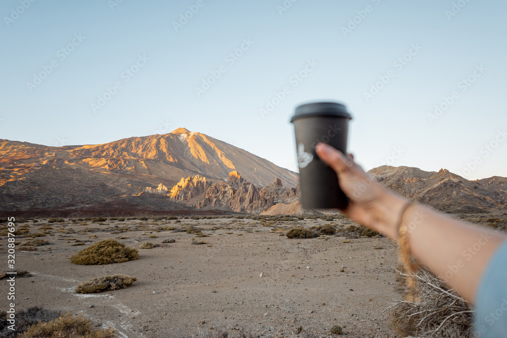 火山谷上拿着外卖咖啡杯的女人，图像聚焦在火山上，伸出了手