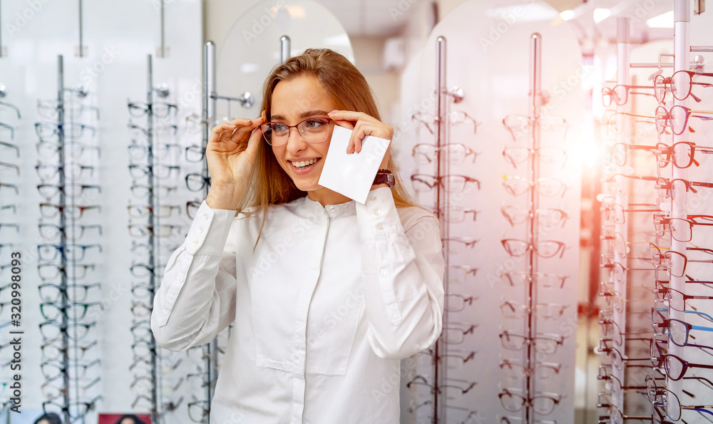 Young beautiful girl in glasses near the stand in the optical store. Emotions. Ophthalmology.