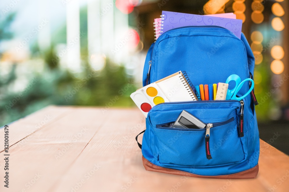 Classic school backpack with colorful school supplies and books on desk.