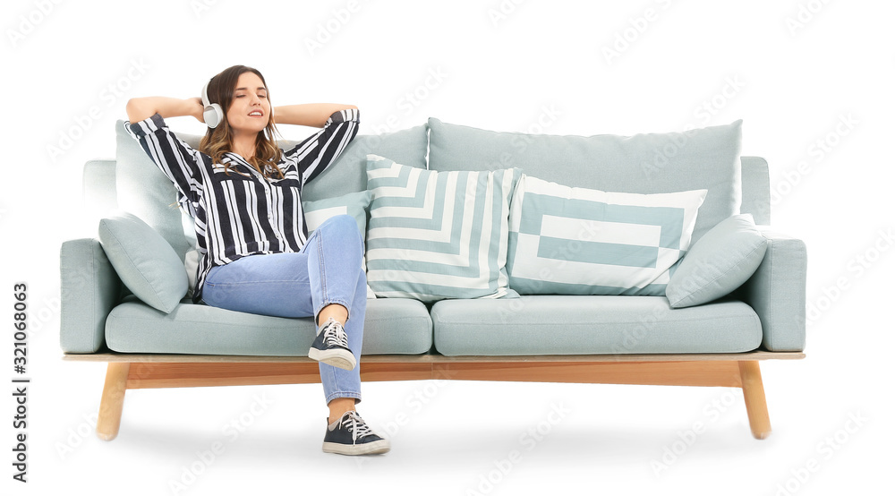 Young woman listening to music while sitting on sofa against white background