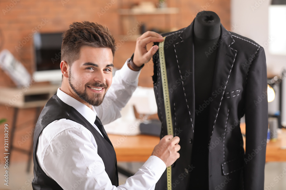 Young tailor taking measurements of male jacket on mannequin in atelier