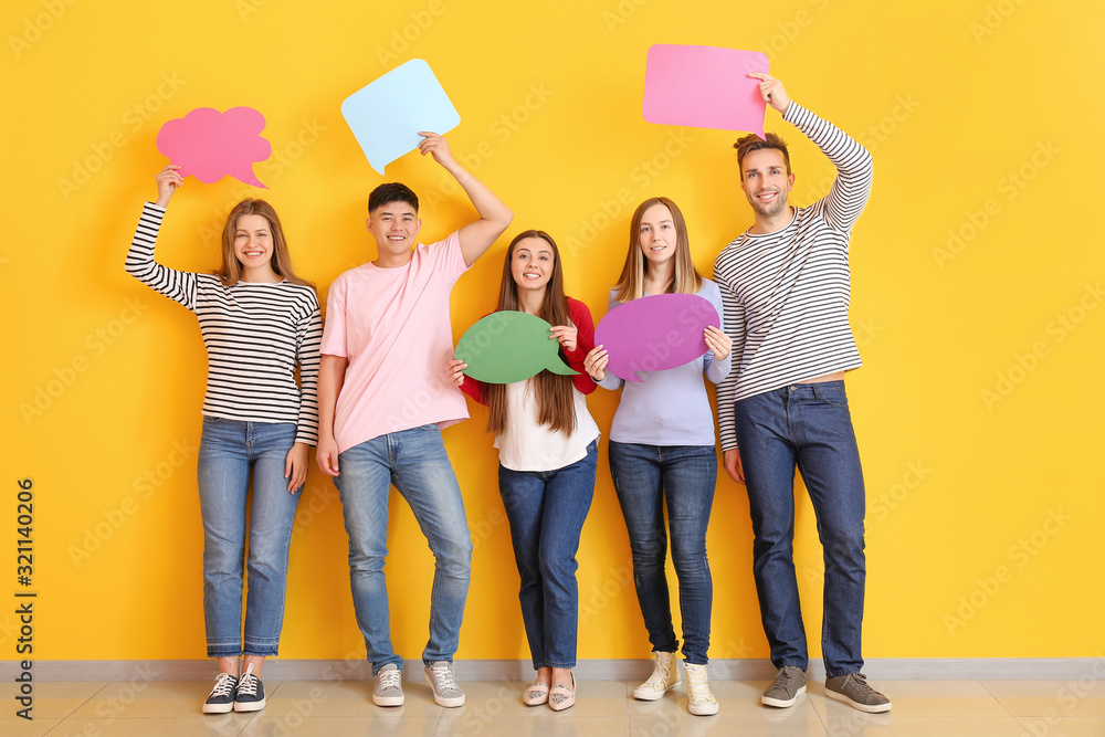 Group of young people with blank speech bubbles near color wall