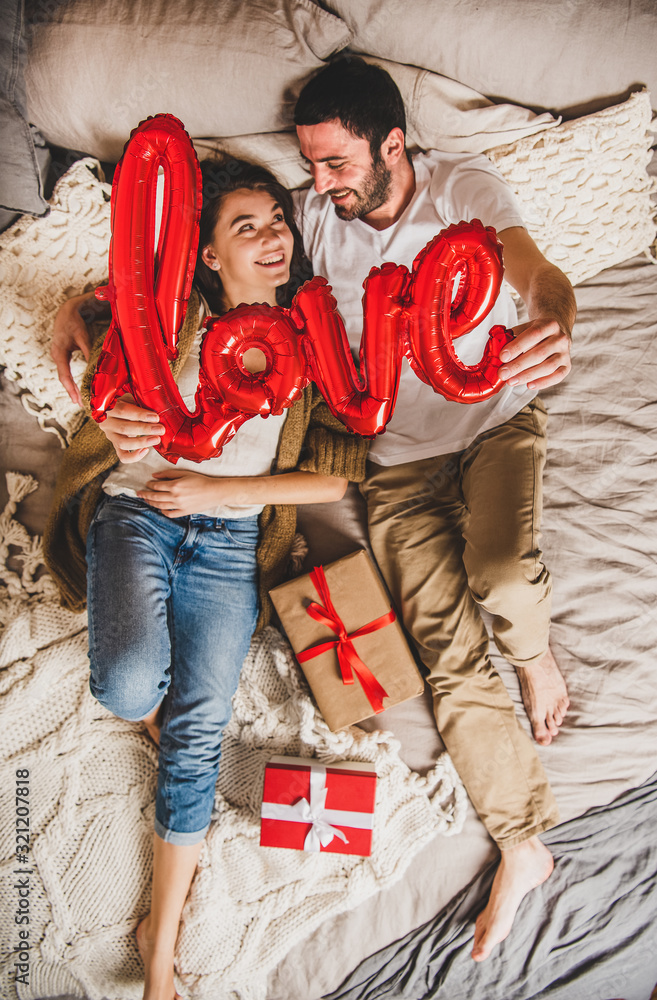 Overhead view of young lovely happy caucasian couple in bed holding red inflated word love with pres