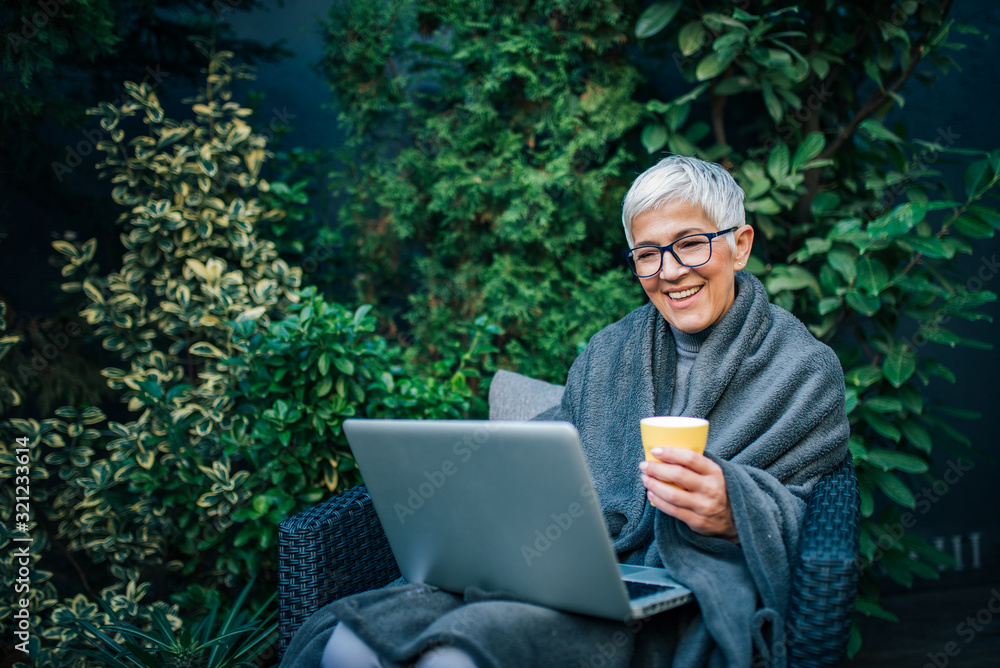 Portrait of a cheerful modern elderly woman using laptop in the garden.