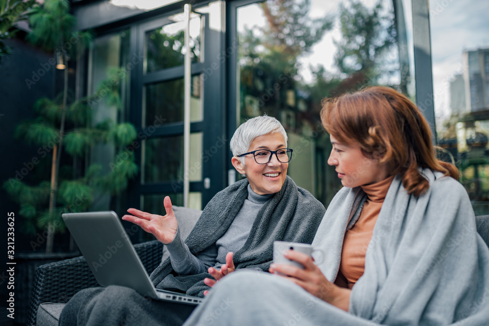 Successful senior businesswoman talking to a mature woman while sitting on the terrace of the modern