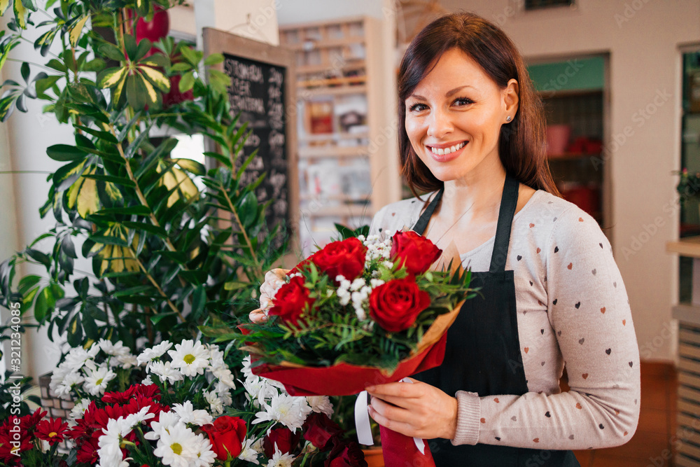 Florist wearing an apron and happily holding bouquet with red roses. Valentines day concept.