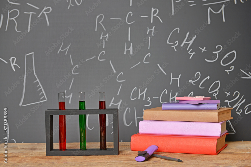 School supplies and test tubes on table near blackboard