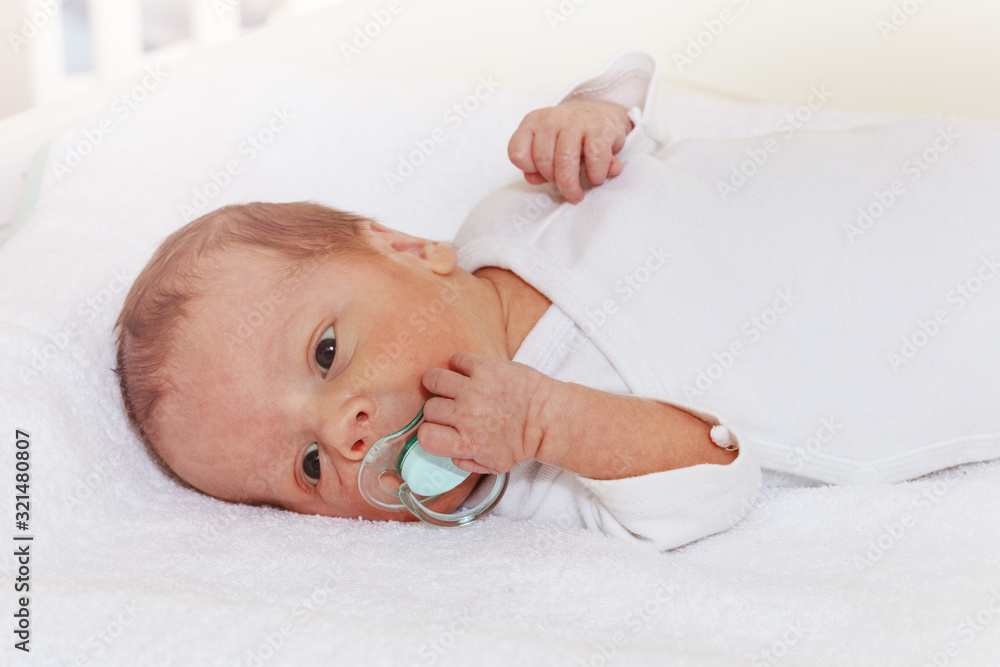 Portrait of little newborn baby boy laying and holding pacifier with hand