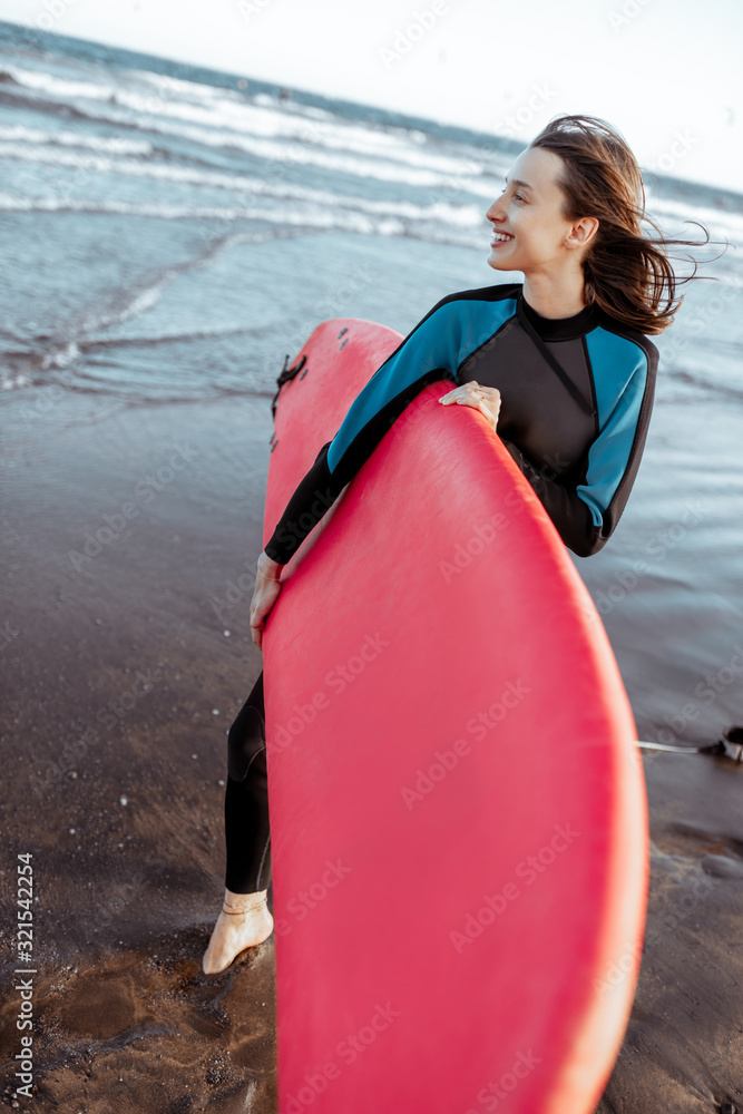 Portrait of a young woman surfer in swimsuit standing with red surfboard on the beach. Active lifest