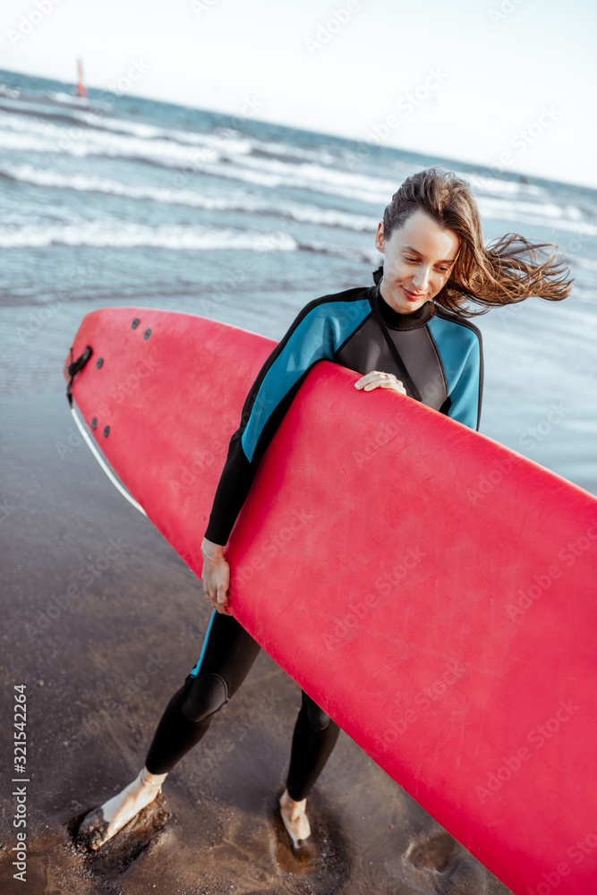 Portrait of a young woman surfer in swimsuit standing with red surfboard on the beach. Active lifest