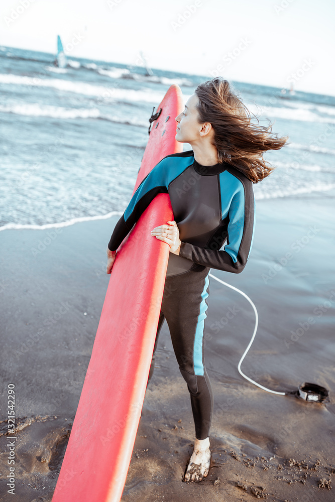 一位穿着泳衣、拿着红色冲浪板站在海滩上的年轻女子冲浪者的肖像。活跃的生活