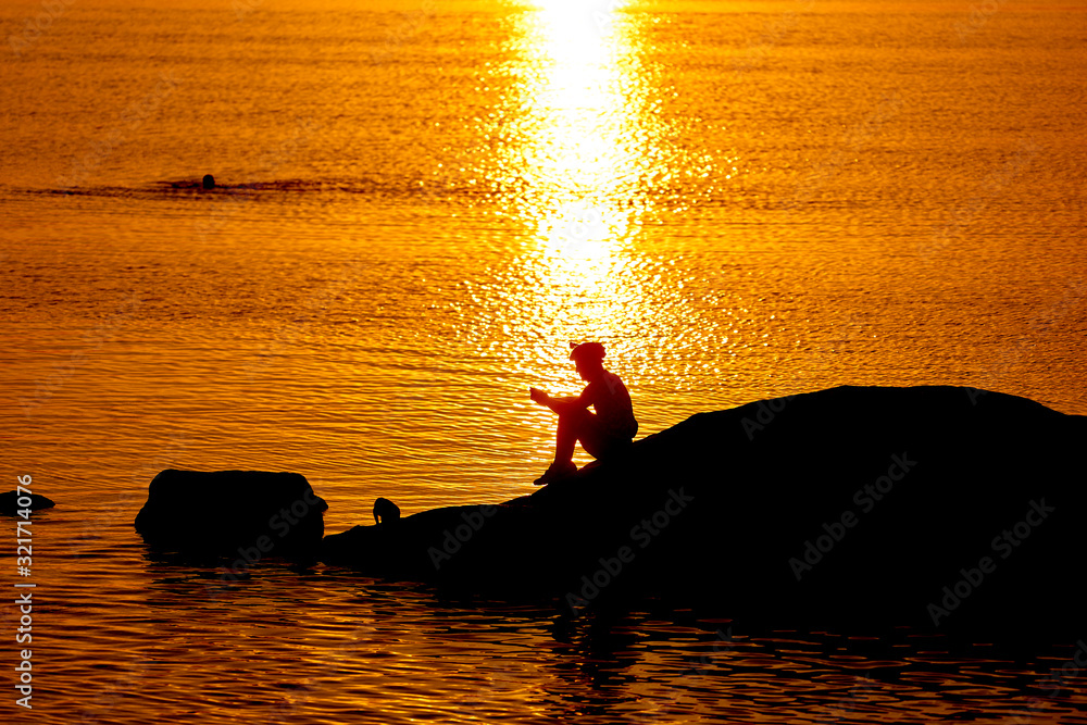 Black silhouette of a cyclist at sunset with a reflection in the water with ripples. Rest on rocks. 