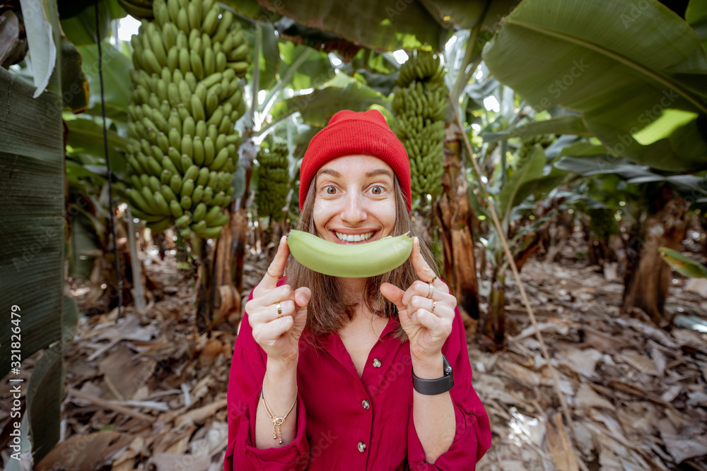 Portrait of a cute woman dressed in red biting banana fruit on the plantation. Fresh fruits eating c