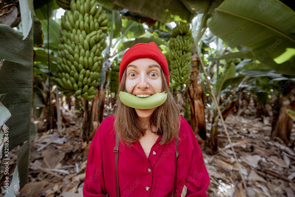 Portrait of a cute woman dressed in red biting banana fruit on the plantation. Fresh fruits eating c