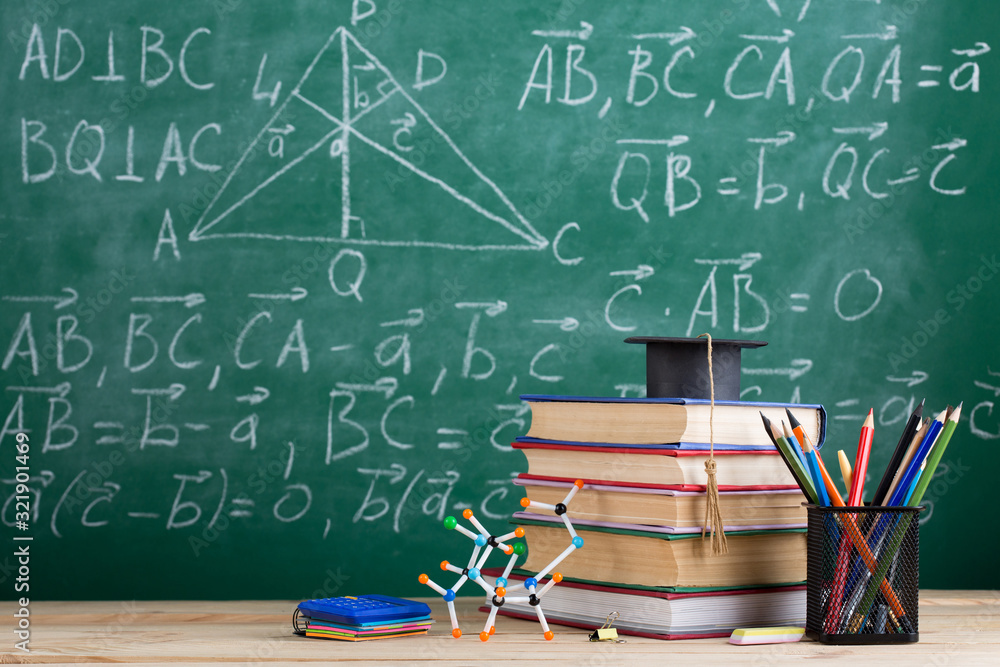 Education and sciences concept - books on the teacher desk in the auditorium, chalkboard on the back