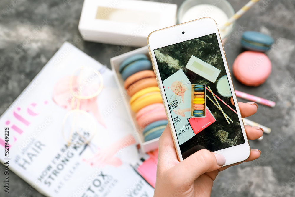 Female food photographer with mobile phone taking picture of macarons and milk