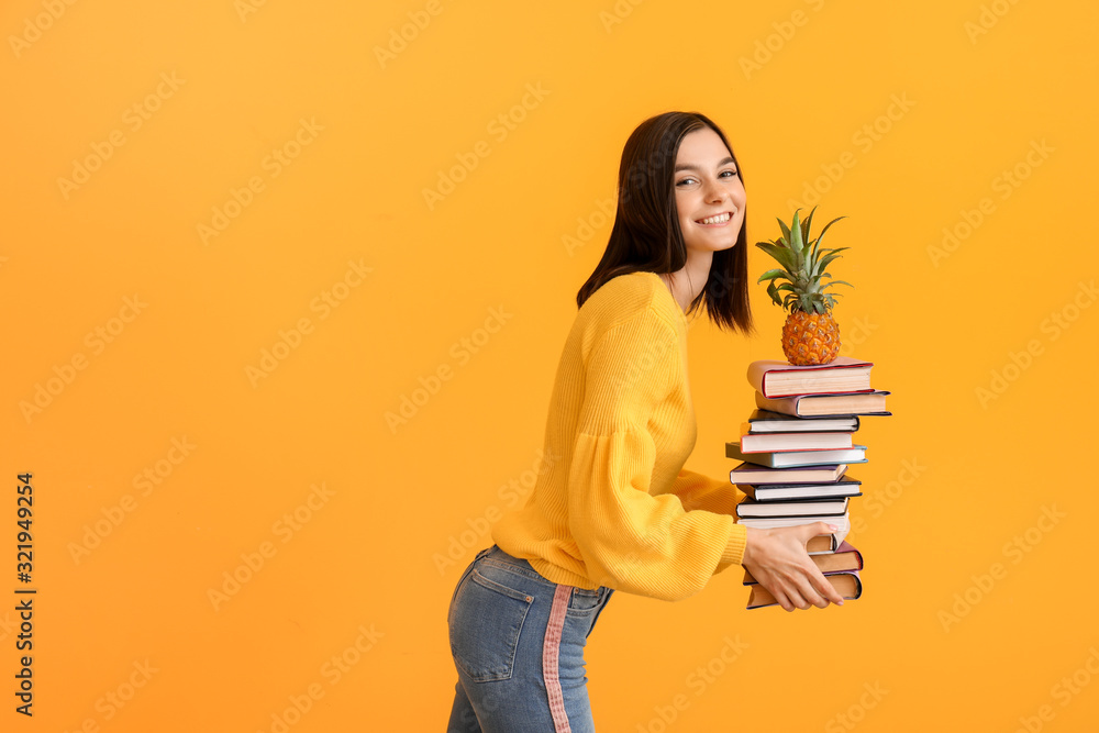 Beautiful young woman with books and pineapple on color background