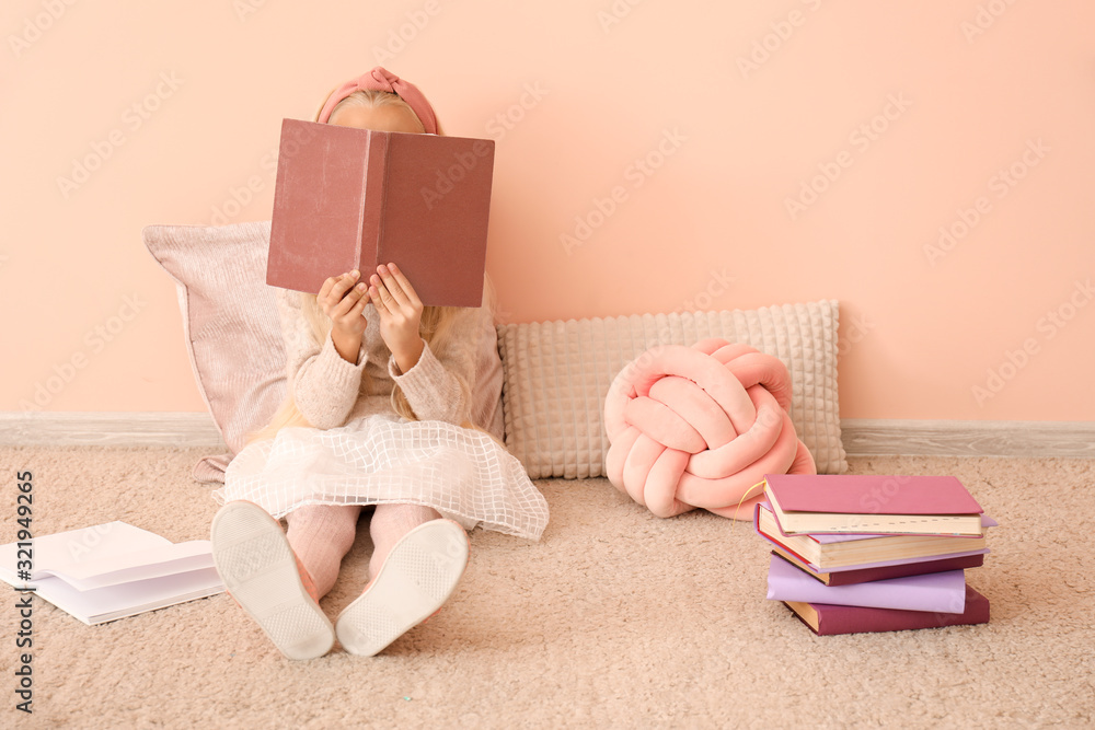 Little girl reading book near color wall