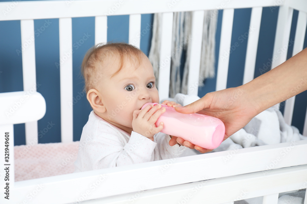 Mother feeding baby with milk from bottle in bedroom