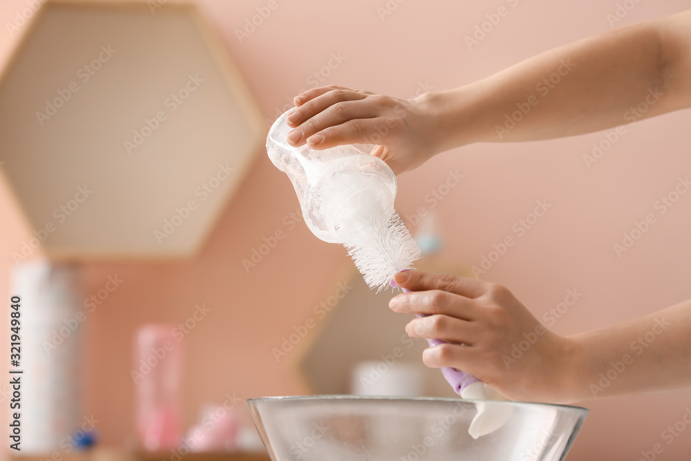 Woman cleaning baby bottle at home, closeup