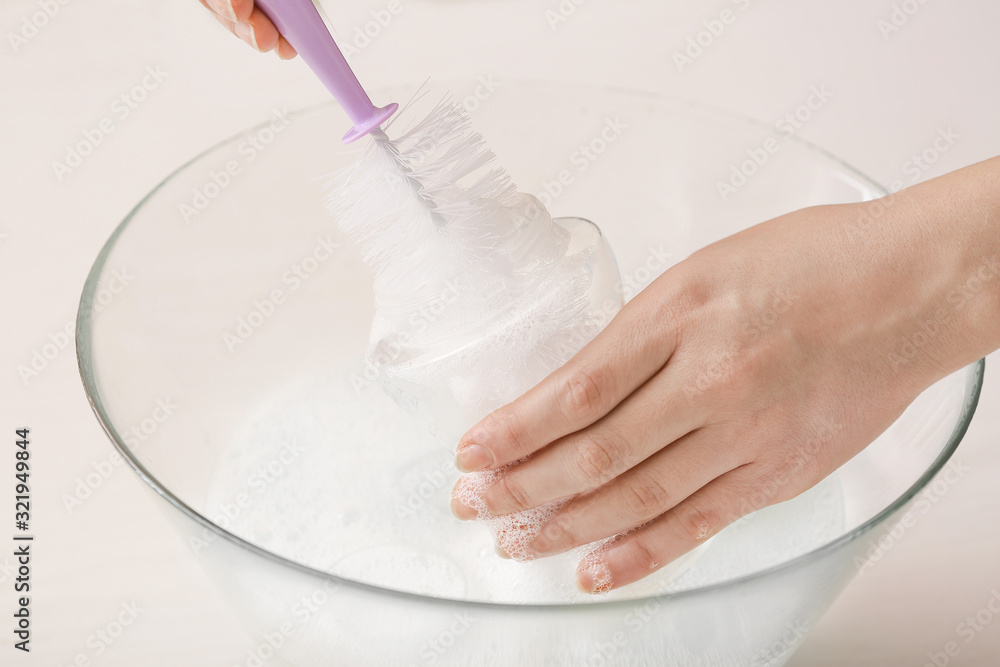 Woman cleaning baby bottle at home, closeup