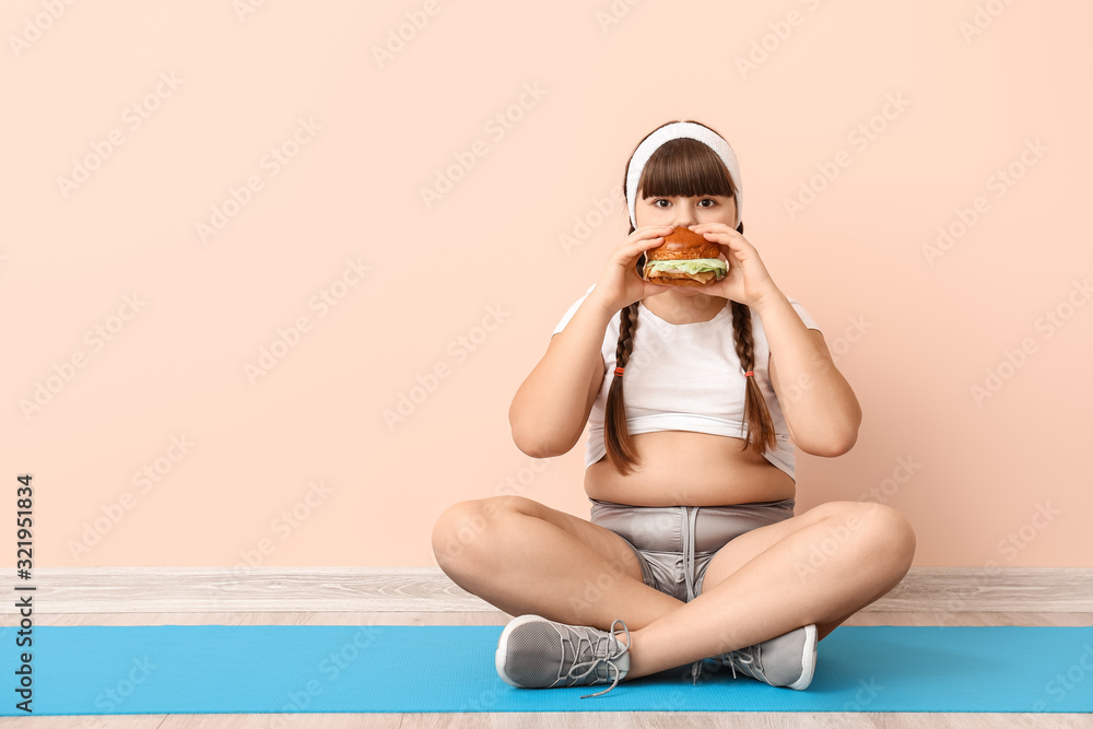 Overweight girl with unhealthy burger near color wall