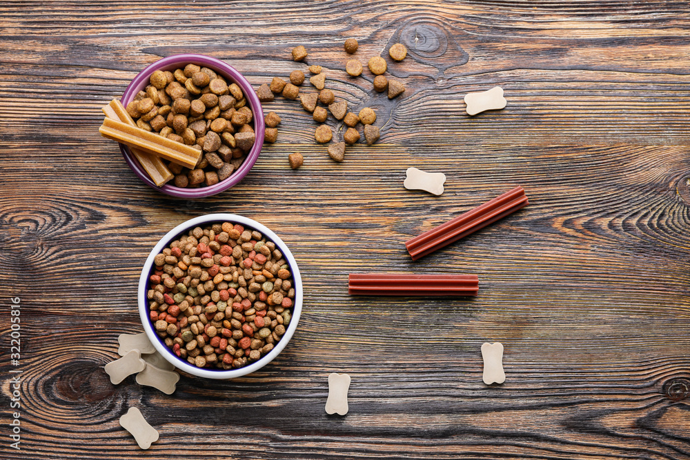 Bowls with dry pet food on wooden background