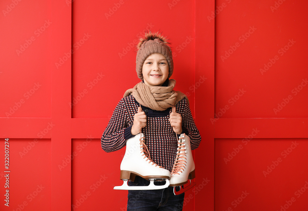 Cute little boy with ice skates against color background