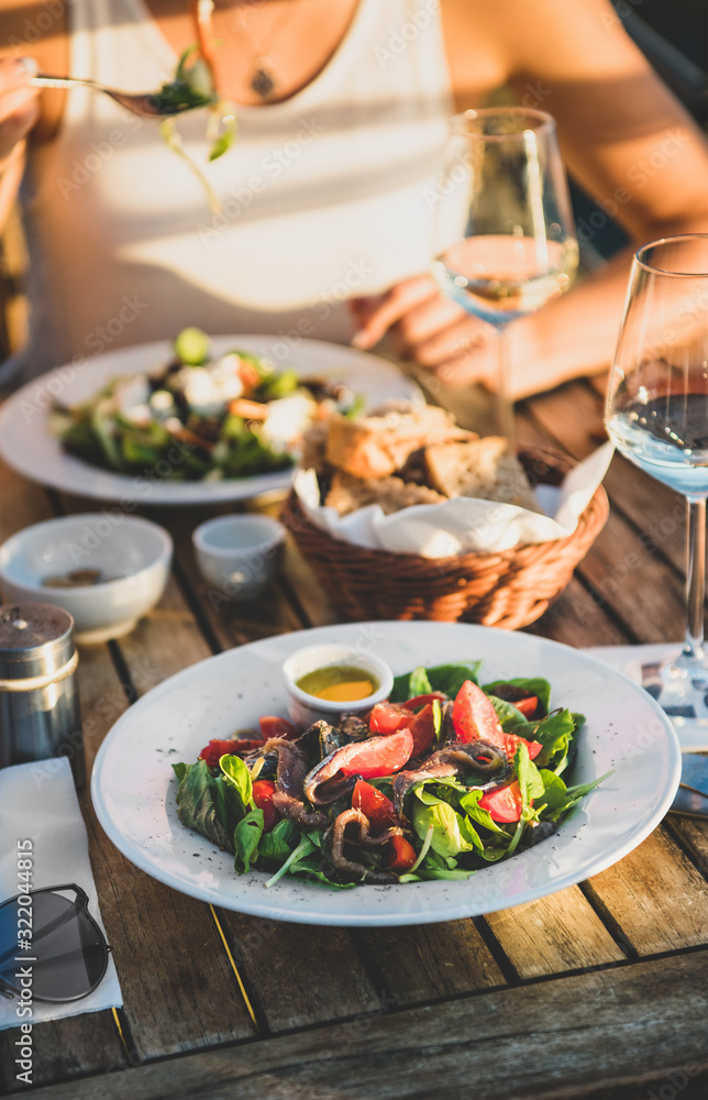 Young woman eating salad with seafood and drinking wine in summer open-air cafe in Italy with pictur