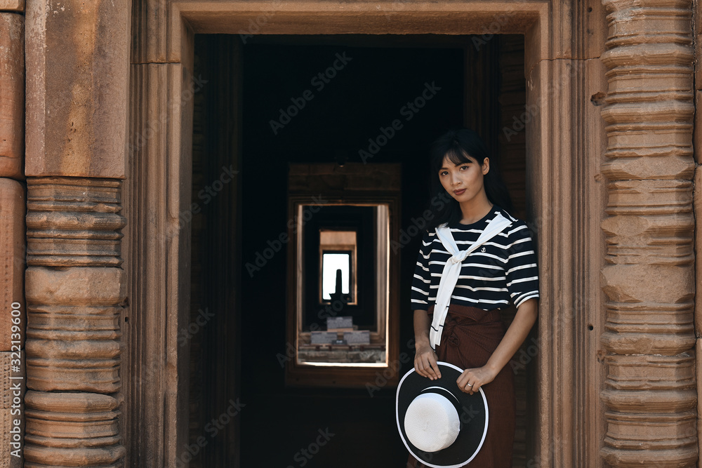 Portrait of young asian thai woman wearing striped shirt and holding white hat in her hands standing