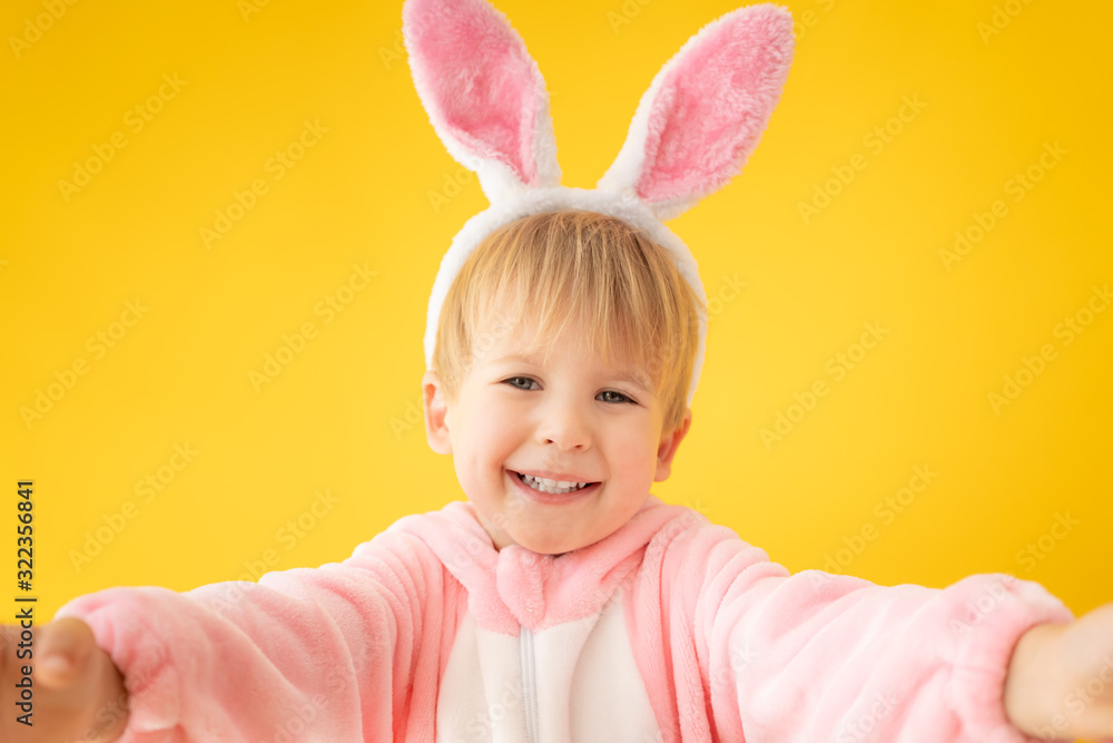 Funny kid wearing Easter bunny against yellow background