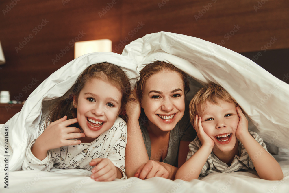 happy family mother and children son and daughter laughing, playing in bed