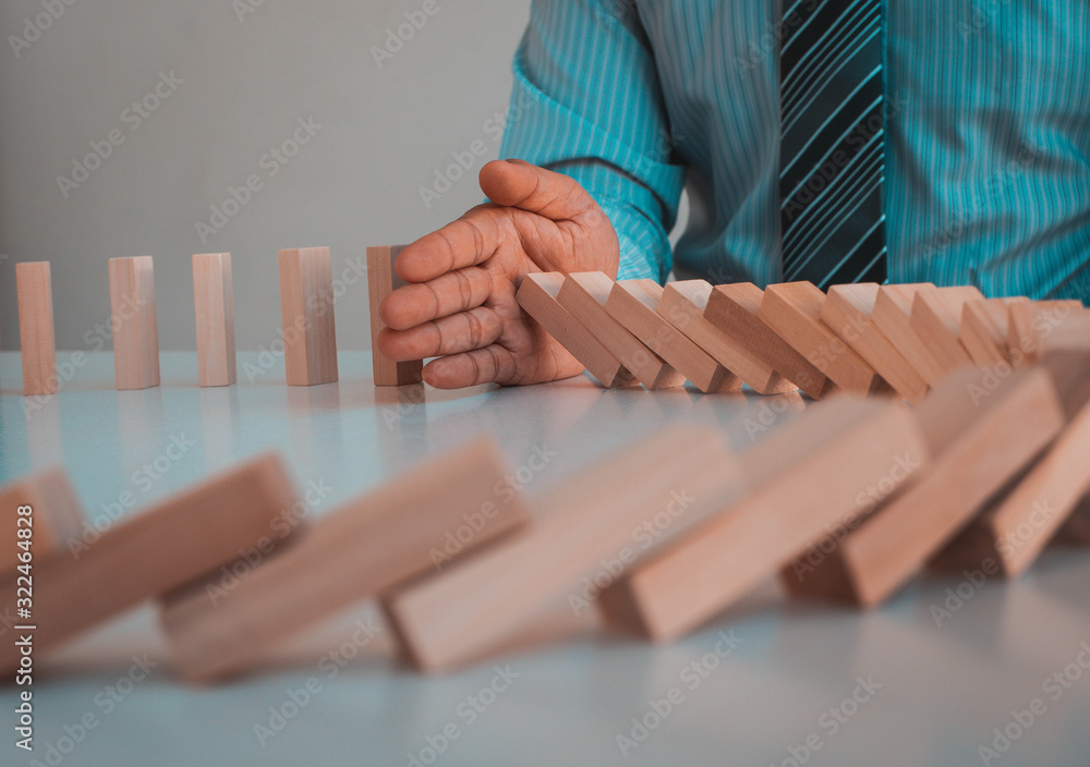 Businessman stopping domino effect with his hand, strategy and successful intervention concept for b