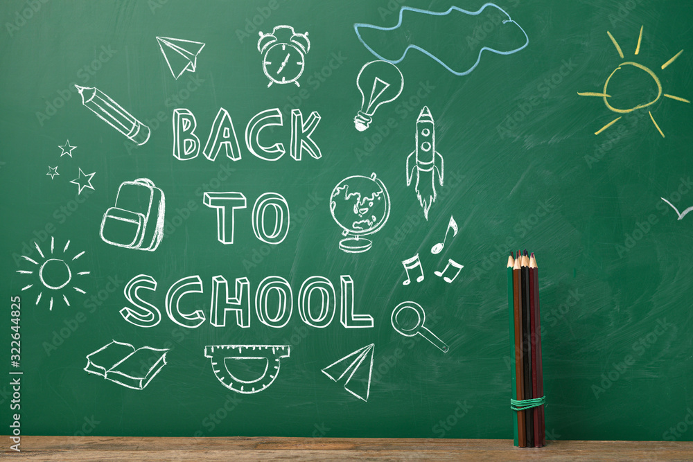 Pencils on table near blackboard with drawings and text BACK TO SCHOOL