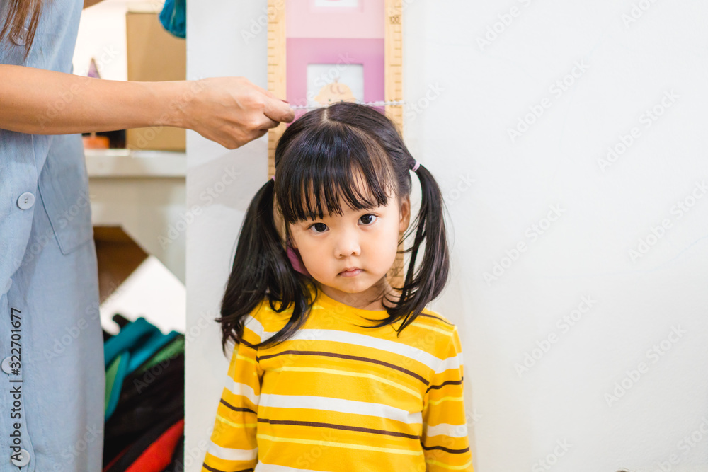 母亲在家里的白墙上给女儿量身高。2.6岁的女孩站着看