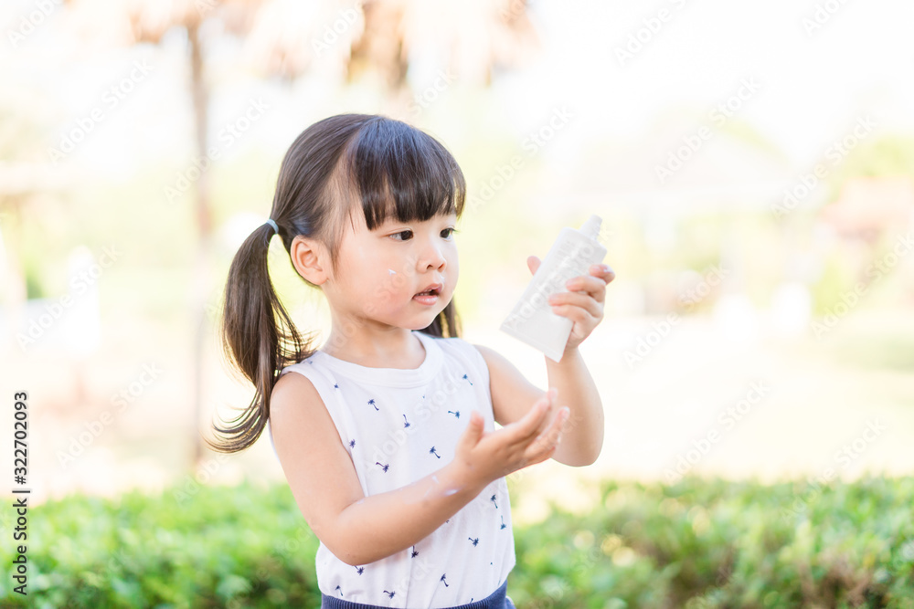 可爱的蹒跚学步的女孩把防晒霜放在胳膊上，在阳光下的池边开心地笑着