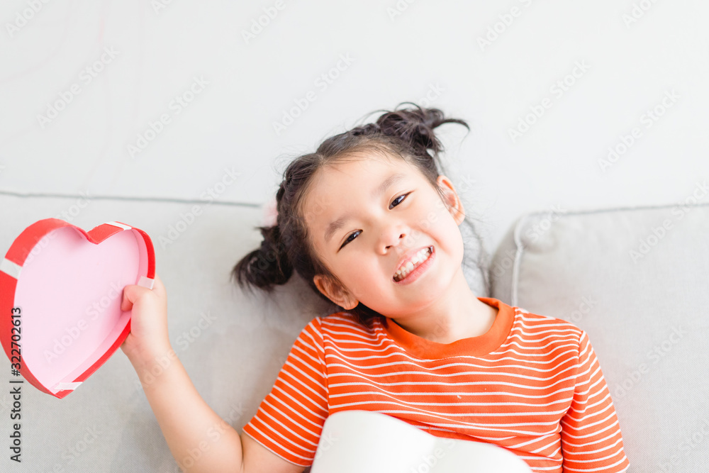 Little asian girl Happy smiley excited face and open red gift box in heart shape in sofa at home on 