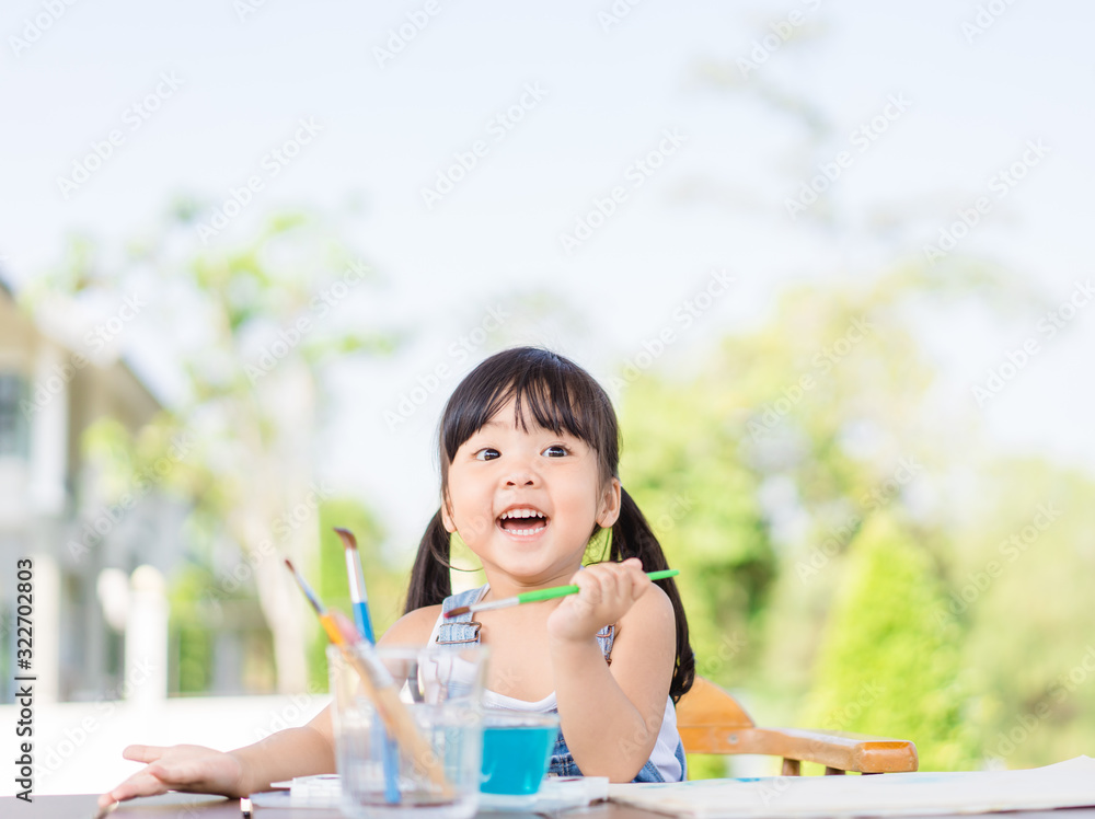 Adorable little asian girl holding a paintbrush and working on a painting watercolor for art class i