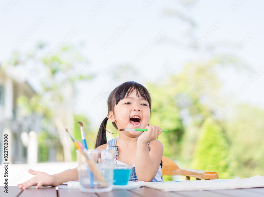 Adorable little asian girl holding a paintbrush and working on a painting watercolor for art class i