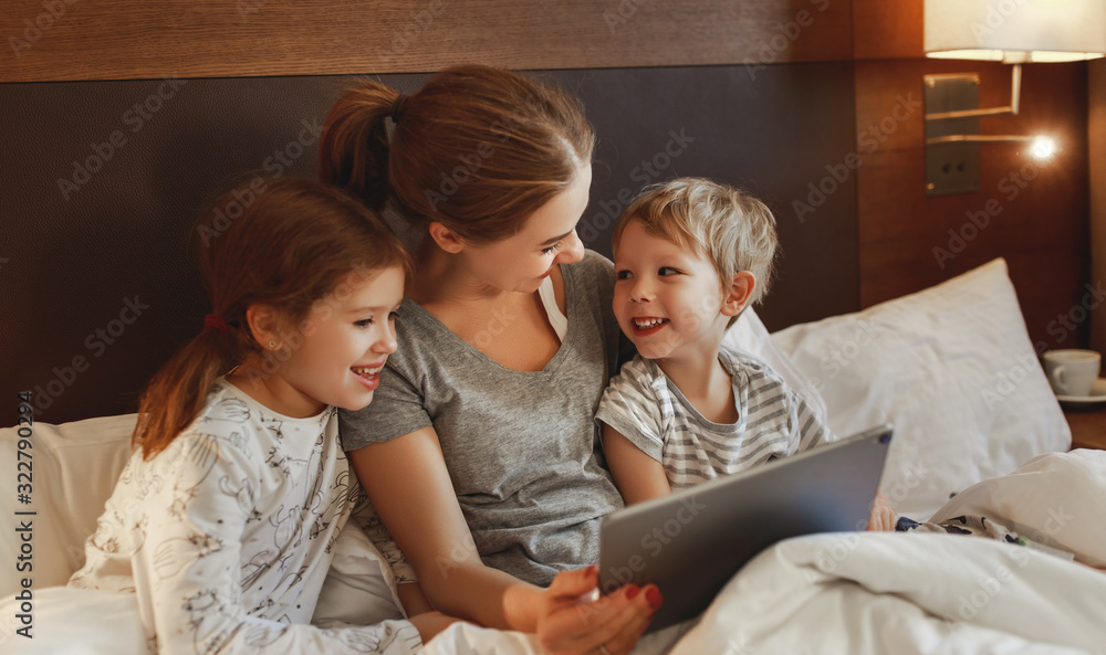 happy family mother and children with tablet computer at home in bed in   evening.