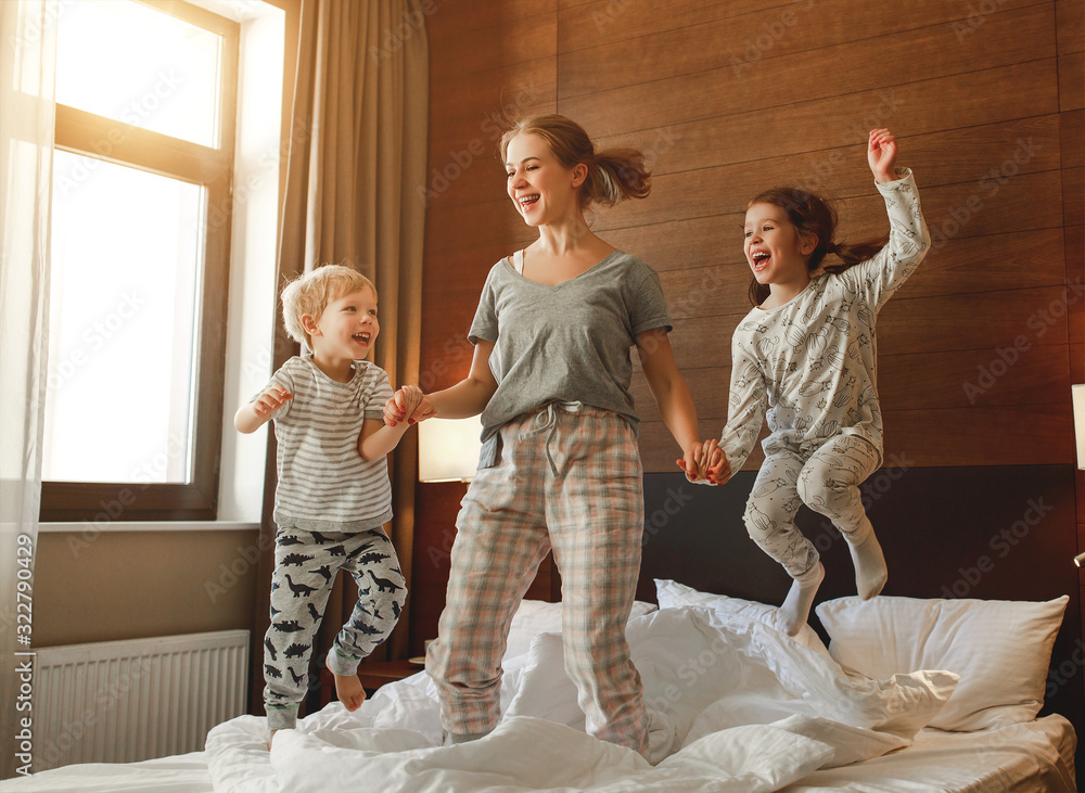 happy family mother and children son and daughter jumping, laughing, playing in bed.