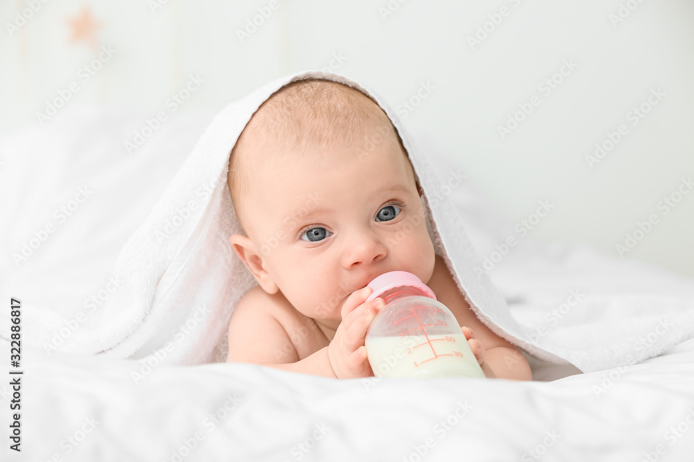 Portrait of cute little baby drinking milk from bottle on bed