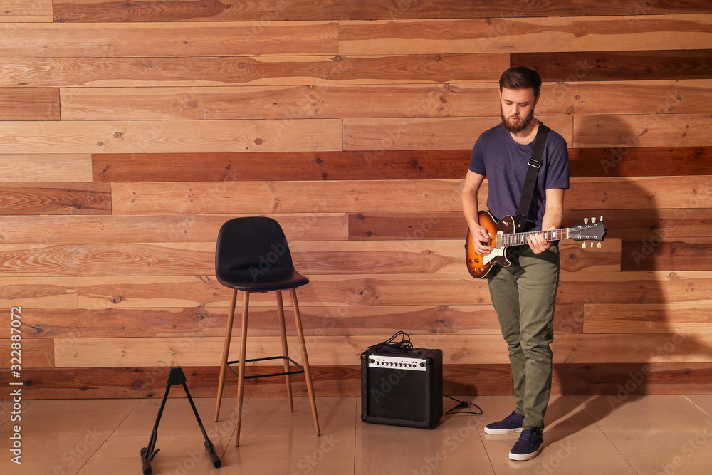 Young man playing guitar near wooden wall